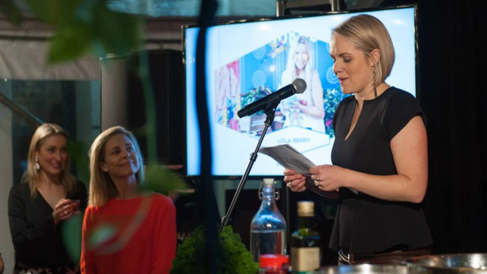 Keito Director Kate Abraham at Nourish Festival giving a speech, with presentation in background.