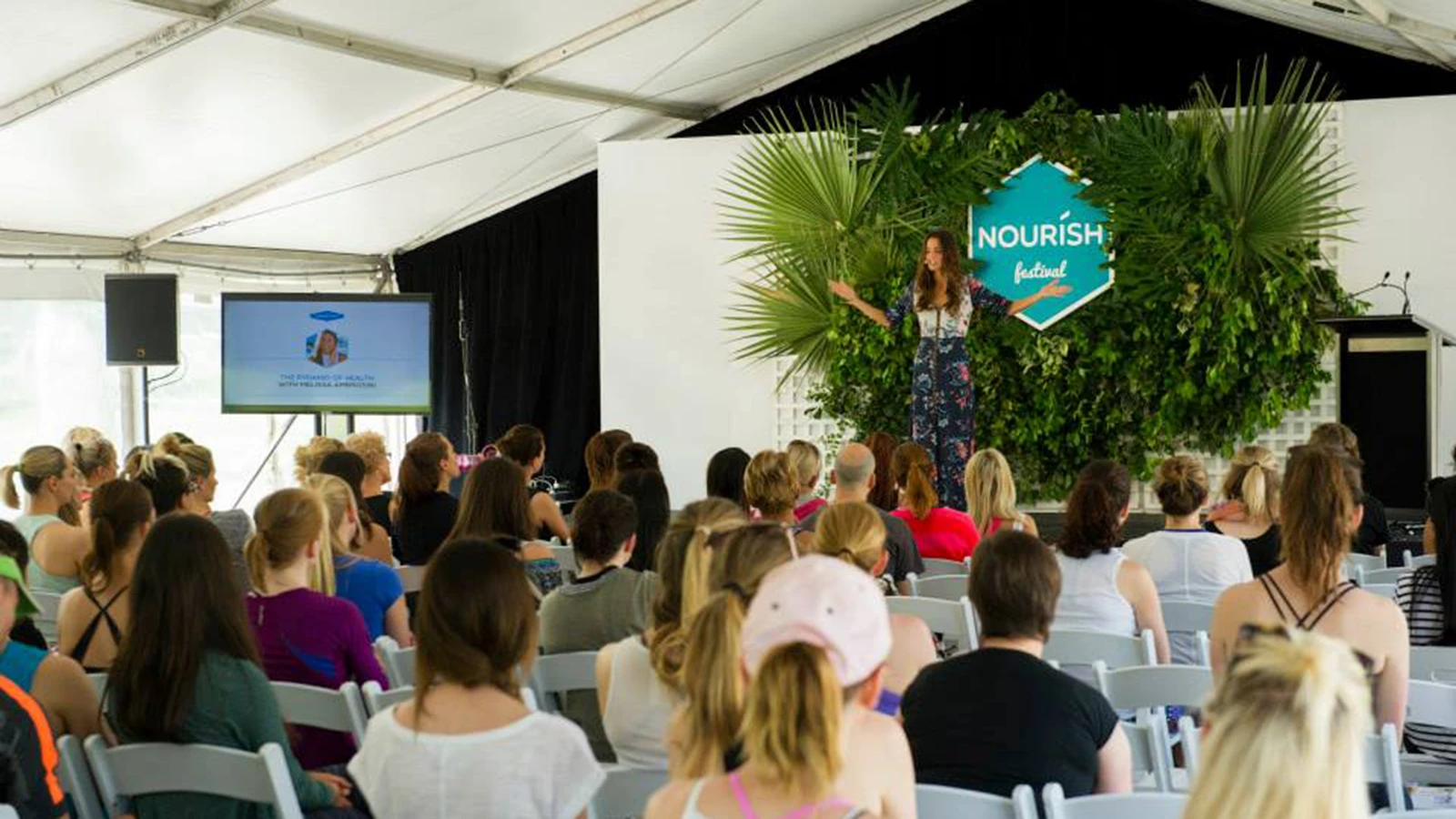 Nourish Festival presentation, signage on stage and presentations in background.