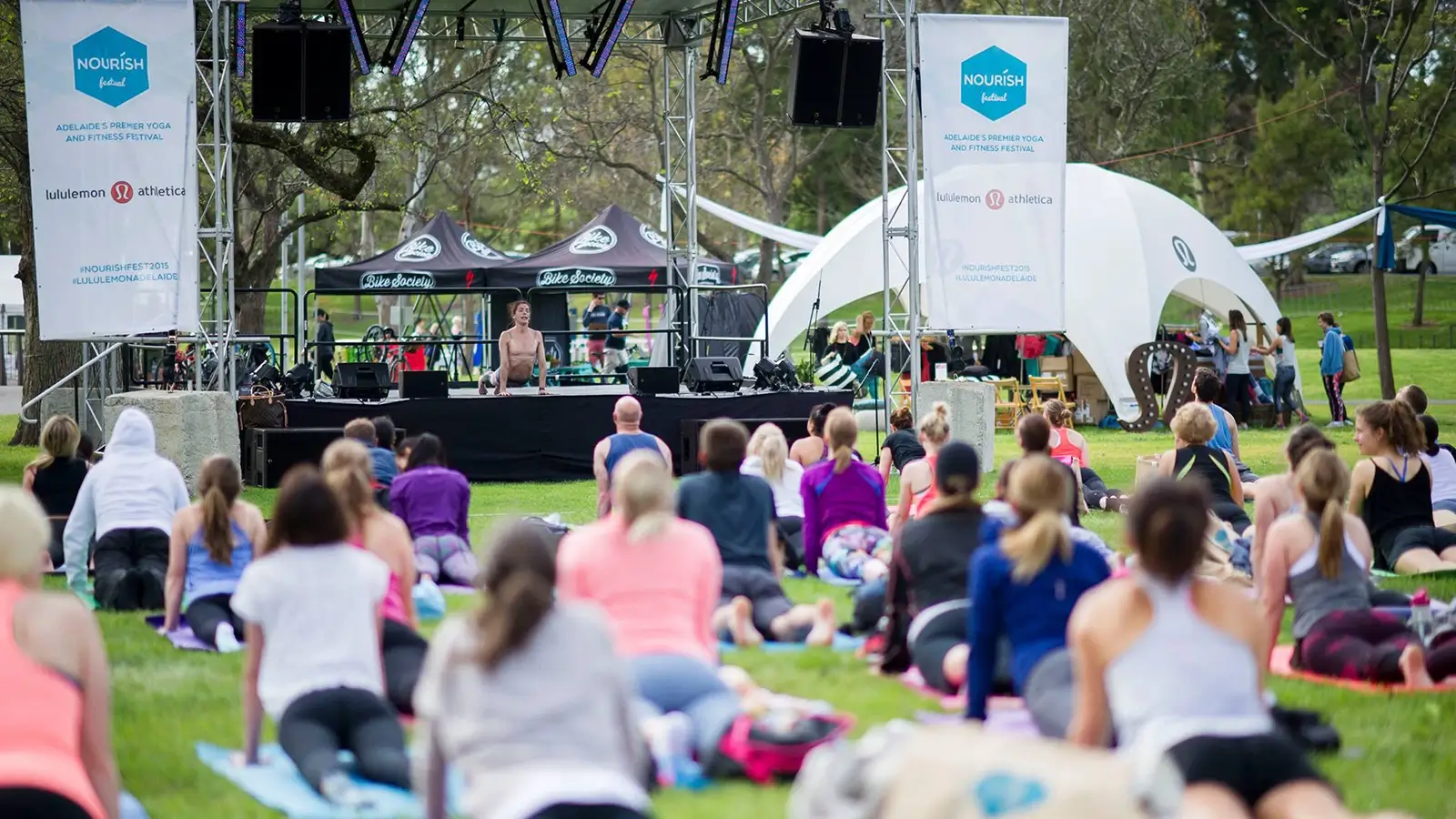 Group yoga at Nourish Fesitval, with event banners on stage.