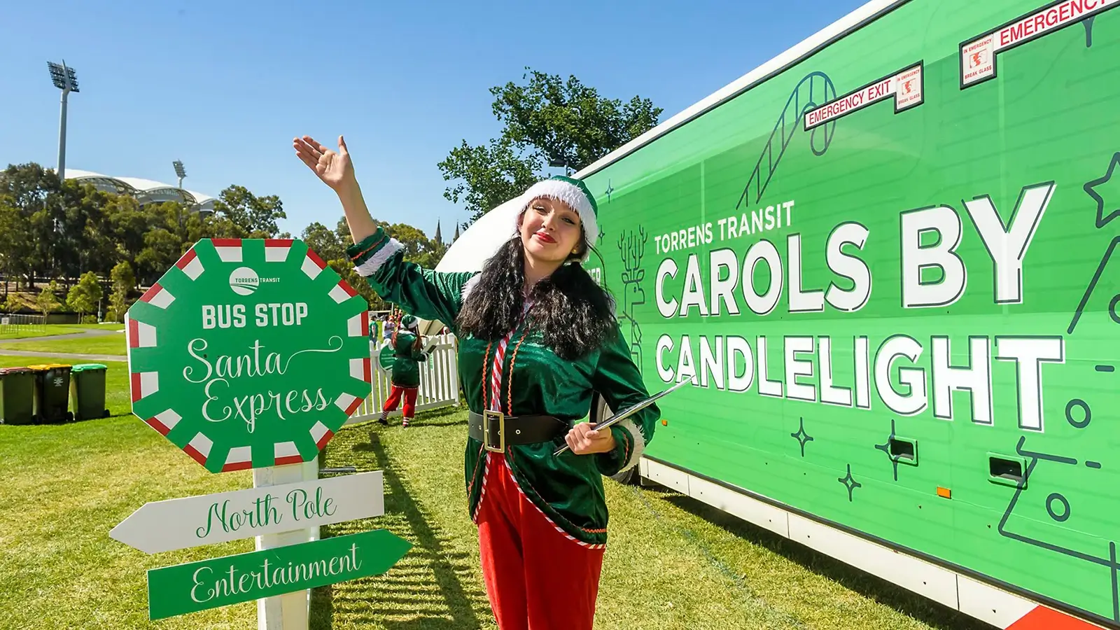 Event signage for Torrens Transit Carols by Candelight Event, bus stop sign with worker in elf costume.